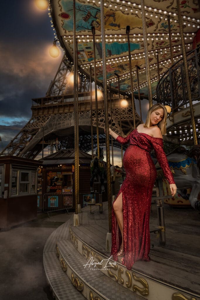 Destination maternity photography images of a pregnant woman in red glittery dress underneath the Eiffel Tower for a babymoon photography experience.